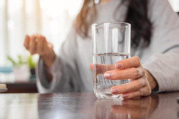 Young woman holding glass of water and taking pill at home.