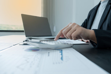 business female is sitting at a desk and use calculator calculating financial graph that show results In the office
