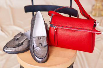 A pair of female shoes of gray color and a red bag on a chair. Beige background.