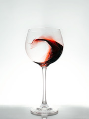 Red wine splashing a wave in a glass.