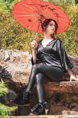 beautiful thin girl in a black Japanese suit and glasses holds a red paper umbrella in a Japanese garden