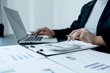 business female is sitting at a desk and use calculator calculating financial graph that show results In the office