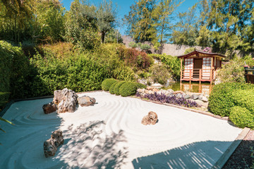 typical japanese zen garden with its drawing area in the sand, a lake, and a small house surrounded...