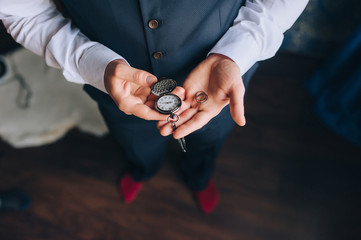 A man, a businessman in a suit holds in his hands a vintage, antique pocket watch and wedding rings close-up. The morning of the groom. Photography, concept, wedding. Clockwork.