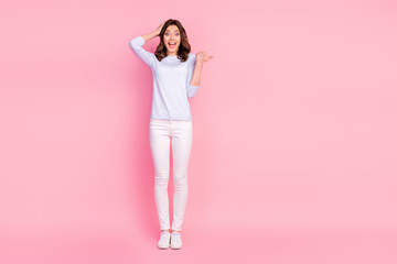 Fototapeta na wymiar Full size photo of attractive shocked lady good mood directing finger empty space showing novelty product wear casual white pullover trousers sneakers isolated pink color background