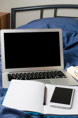 Laptop and smartphone, coffee cup and notebook on the bed in morning time. Mock up.