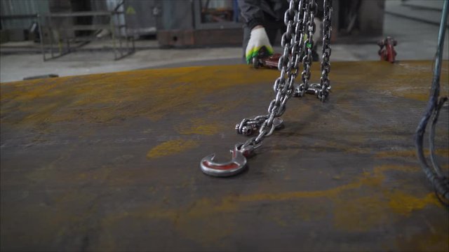 A worker hooks a rope hook onto a metal sheet. A worker hooks a sling to metal steel.