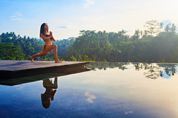 Good morning with yoga meditating on sunrise background. Active woman in bikini practicing at villa...