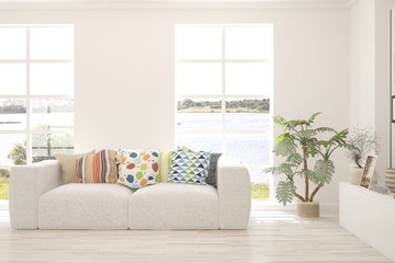Fototapeta premium White living room with sofa and summer landscape in window. Scandinavian interior design. 3D illustration