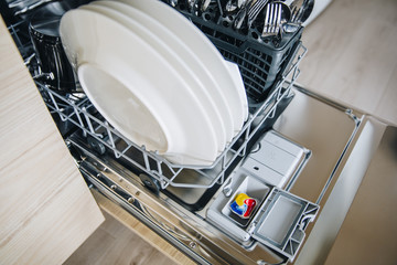 Colorful dishwasher detergent tablet for dishwashing machine. Open dishwasher with clean glasses...