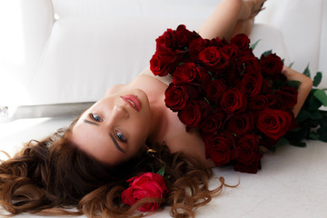 The brunette is lying on the white floor, with a large bouquet of red roses.