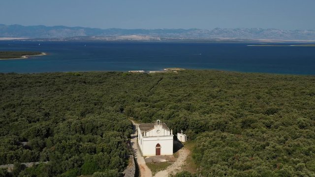 The Ancient Church Of Saint Roch In Olib Island, Croatia Surrounded By Green Trees On A Sunny Day - aerial shot