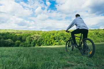 A man on a bicycle resting looks at the nature in the forest on a sunny day