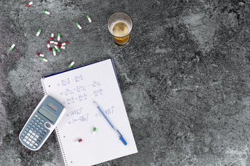 the excessive consumption of alcohol, drugs and medicines damages health and hinders learning, hand-written notes. calculator beer glass and pills on a grey marble table
