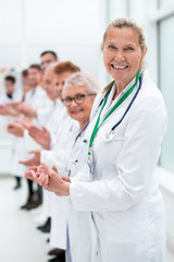 smiling female doctor standing in front of her applauding colleagues.