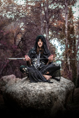 Woman in the forest dressed in a tunic as a sorceress holding a large sword
