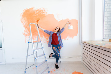 Repair in the apartment. Happy woman paints the wall with paint.