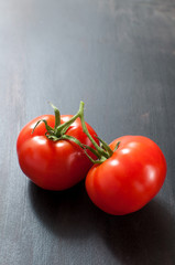 a pair of two fresh organic tomato on dark grey background, vertical image