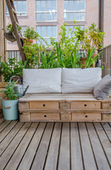 Wooden pallet couch on balcony with plants in background