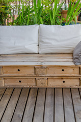 Fototapeta na wymiar Wooden pallet couch on balcony with plants in background