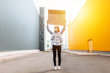 woman in a medical protective mask holds a cardboard placard with the words STOP the virus, on a street in the city