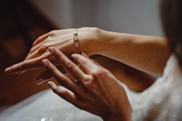 Beautiful elegant bride puts a bracelet on her hand, closeup. Girl put a bracelet on arm.Preparing the bride for the wedding ceremony. - obrazy, fototapety, plakaty