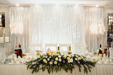 Festive table decorated with winter composition of with fur tree branches in the banquet hall. Table newlyweds in the banquet area on party. Christmas winter wedding. Film noise
