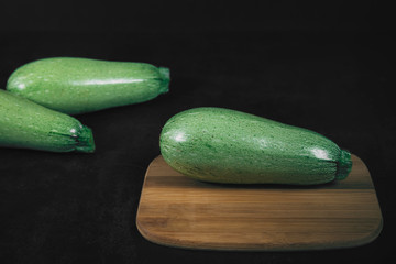 Three green squash on wooden brown board on a black background. Organic eco food. Healthy diet. Freshly picked vegetables. Fresh greens for salad. Natural organic food. Edible vegetable background.
