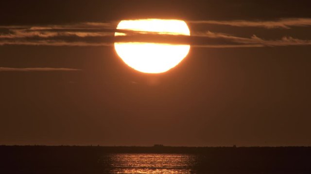 Traffic and pedestrians under huge setting sun over ocean