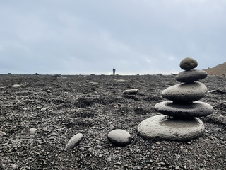 stones stacked on black beach and person on the horizon
