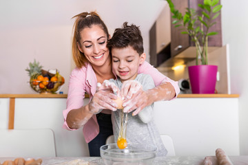 Obraz na płótnie Canvas Young mother and cute little son boy preparing the dough, bake cookies and having fun in the kitchen. Happy family are preparing bakery together.