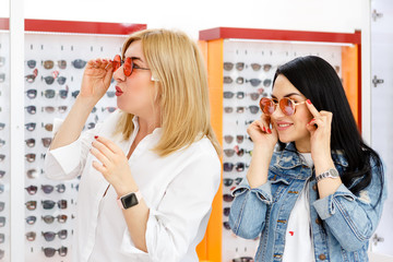Two beautiful girls in the optics store choose new sunglasses