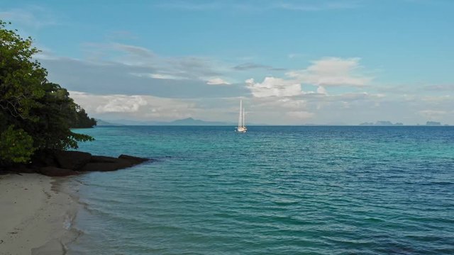 White two-masted yacht anchoring in a bay of tropical island - Koh Kradan in Thailand; dolly shot.