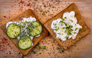 Healthy sandwiches with cream cheese, pea and linen microgreens, cucumber slices and spices on cutting board. Healthy eating, diet vegan food. Top view.