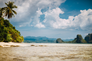 Fototapeta premium El Nido, Palawan, Philippines. Scenic tropical landscape of shallow lagoon, sandy beach with palm trees. Exotic islands and white cloudscape in background