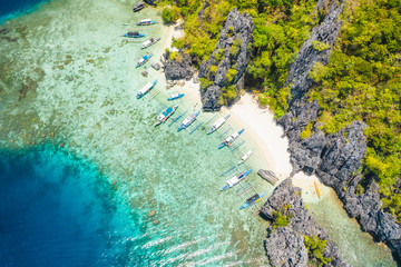 Aerial view of day trip boats moored at tropical Shimizu Island. Limestone coastal rocks, white sand beach in blue water. El Nido, Palawan, Philippines