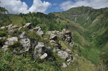 Mountains on the horizon, rock fragments and grass on top of one of the mountains and a valley below