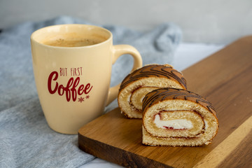 Two slices of sponge roll on wooden cutting board and a cup of coffee