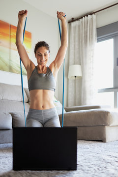 Woman Doing Shoulder Press Workout With Rubber Bands While Looking At Her Laptop. Straight Arms