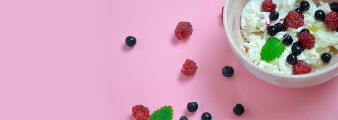 Ricotta with fresh berries and honey on pink table. Cottage cheese, curd cheese or tvorog with berries in bowl. Summer dessert, breakfast healthy keto diet, fitness nutrition banner, top view.