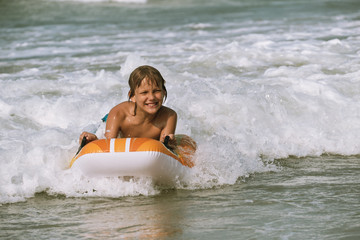 Happy with life, portrait of the caucasian tanned boy rolling on the wave towards the shore on the bodyboard