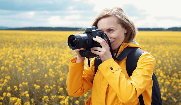 Female photographer taking shots using digital camera standing on blooming rapeseed field background