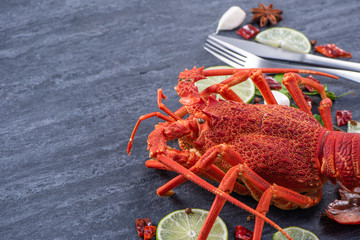 Cooked boiled lobster, delicious dinner seafood meal set with knife and fork on black stone slate background, restaurant menu design, close up, overhead