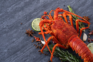 Cooked boiled lobster, delicious dinner seafood meal set with knife and fork on black stone slate background, restaurant menu design, close up, overhead