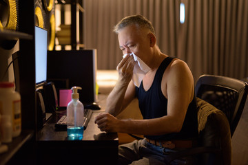 Stressed mature Japanese man getting sick while working from home