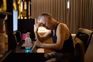 Stressed mature Japanese man having headache while working from home