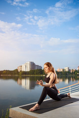 Fototapeta na wymiar Young woman doing yoga near the water, leading healthy lifestyle in nature, time to relax in the morning at the sunrise, meditation on the mat, copy space