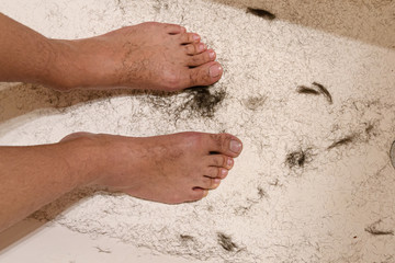 The legs of a man in a white bathtub, there is a lot of shaved hair around. The process of shaving legs.