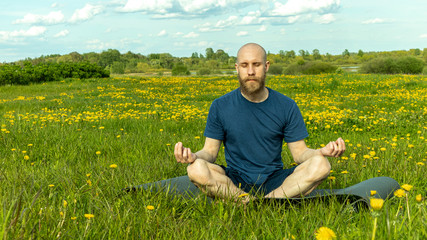 A bald man with a beard meditates in nature