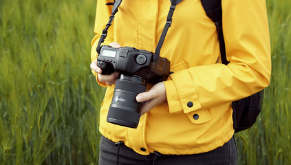 Midsection of impersonalized woman standing on spring grain field background holding digital camera